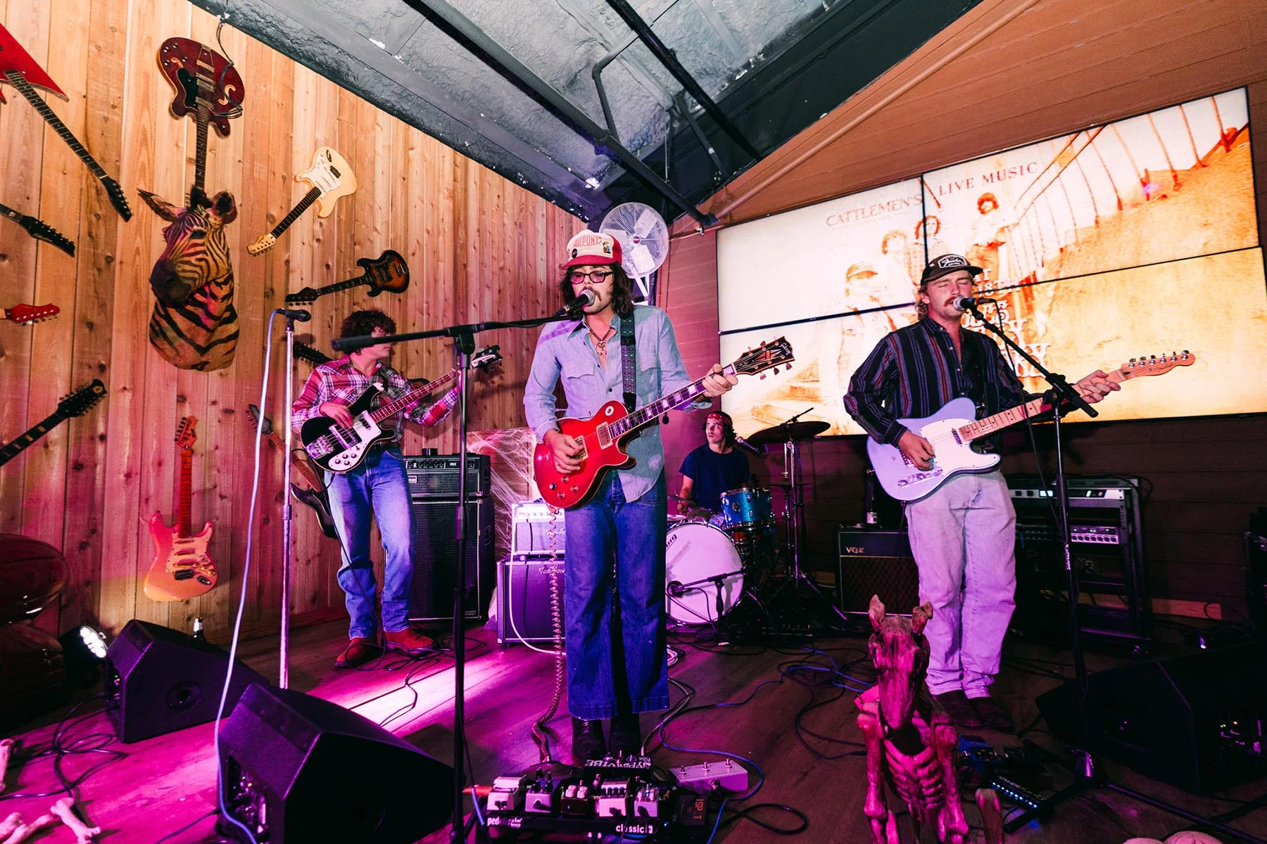 A band mid-set under magenta stage lighting at Cattlemen's Country Club, guitars mounted on the wall behind