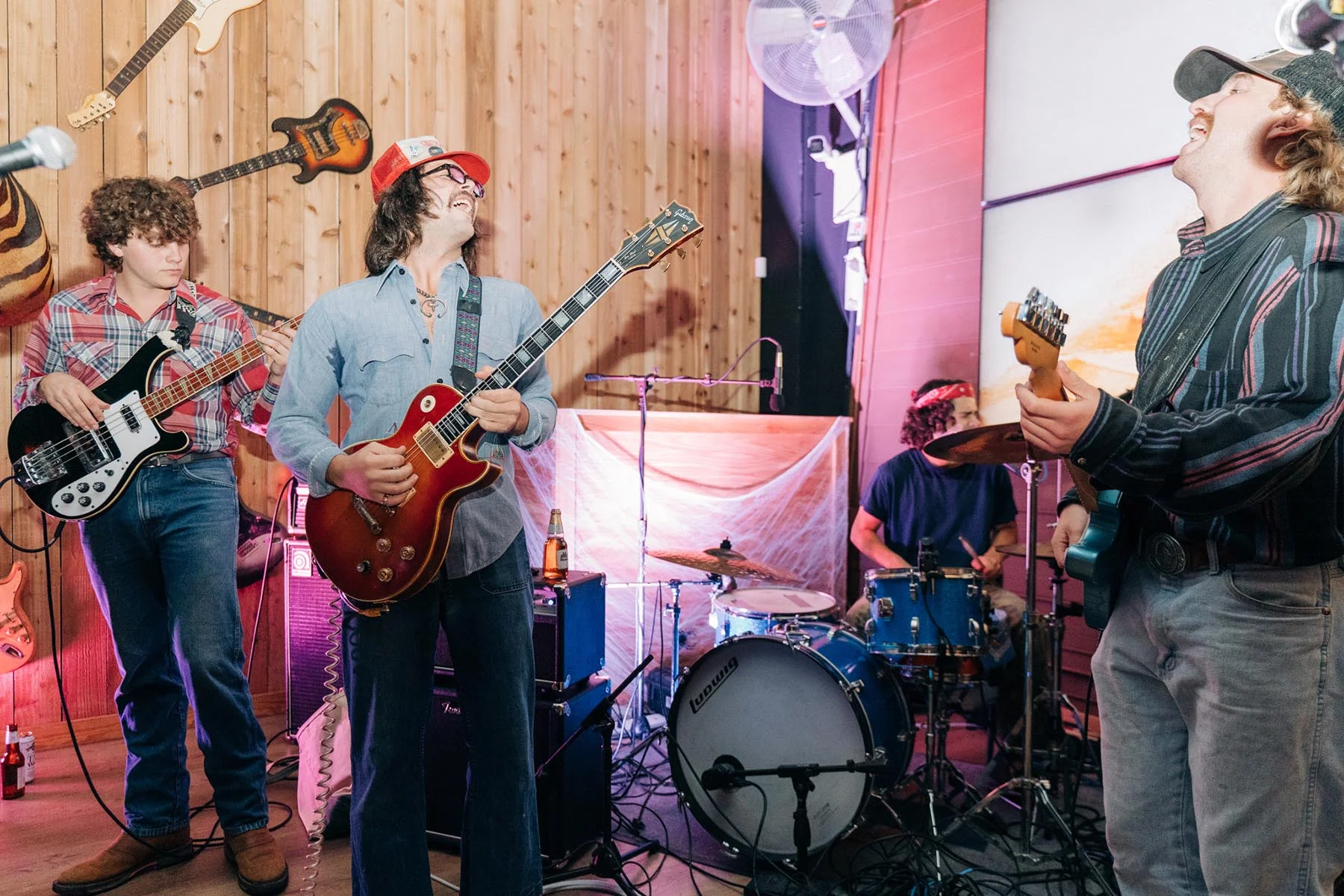 A full band on stage at Cattlemen's Country Club — drums, guitars and vocals against the wood-panelled wall