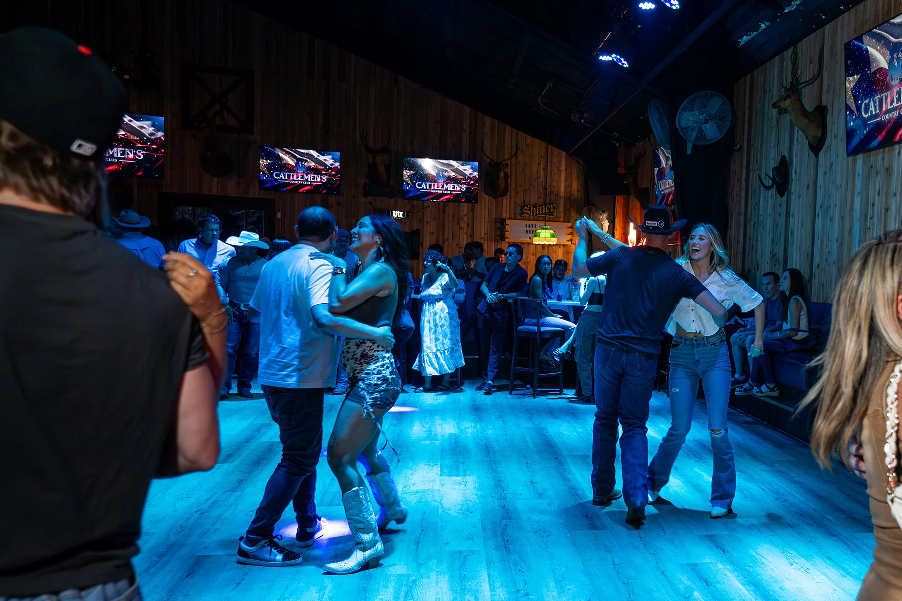 Parejas bailando country swing en la pista de Cattlemen's Country Club, bajo luces azules